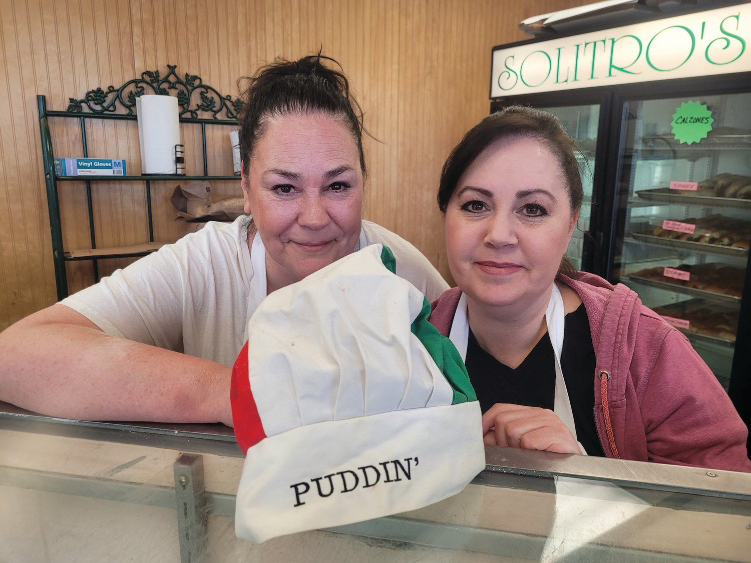 BIG HAT TO FILL: Current owner of Solitro’s Bakery, Elena Pennacchini, and her sister, Diane Notarianni, pose for a photo with their late father’s “PUDDIN’ Hat.”